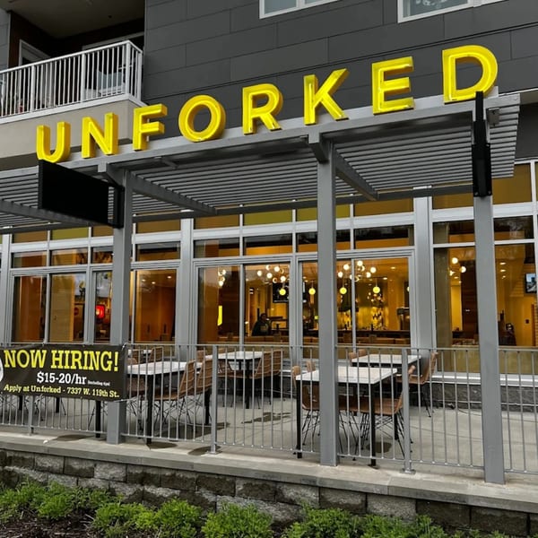 Unforked restaurant exterior with yellow neon sign, outdoor patio seating, and a "Now Hiring" banner.