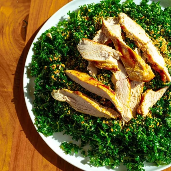 Grilled chicken slices on a bed of vibrant green kale salad with golden breadcrumbs.