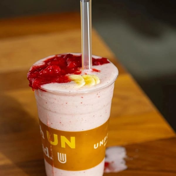 Unforked strawberry banana smoothie with whipped cream and strawberry topping, on a wooden table.