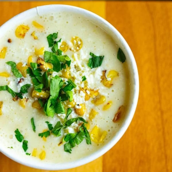 Unforked's creamy corn soup, garnished with fresh cilantro and cotija cheese, in a white cup.