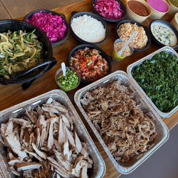 A buffet of burger toppings including shredded chicken, pork, kale, various salsas, and sauces.