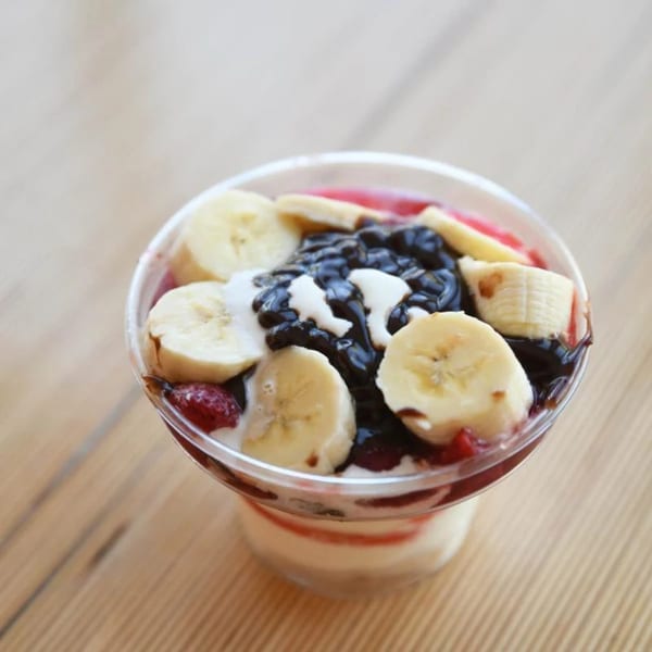 Unforked's fruit parfait with bananas, blueberries, strawberries, and cream on a wooden table.