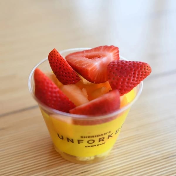 Unforked fruit cup with strawberries and melon, on a light wooden surface.