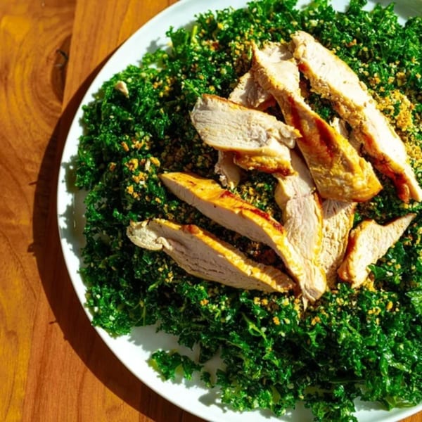 Grilled chicken slices on a bed of vibrant green kale salad with golden breadcrumbs.
