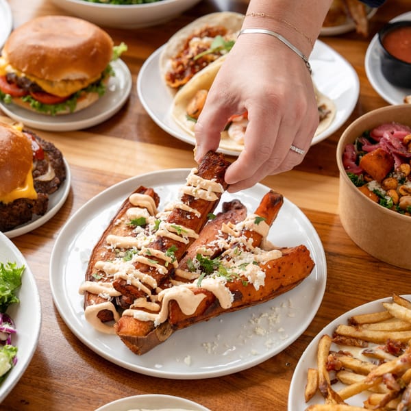 A hand picks up a sweet potato fry from a plate of Unforked burgers, tacos, and fries.