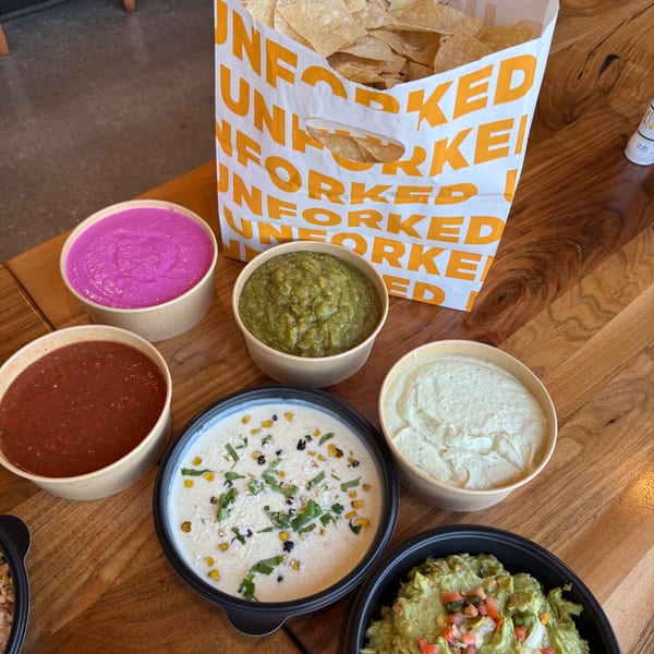 Unforked chips and various dips, including salsa, guacamole, and queso, on a wooden table.