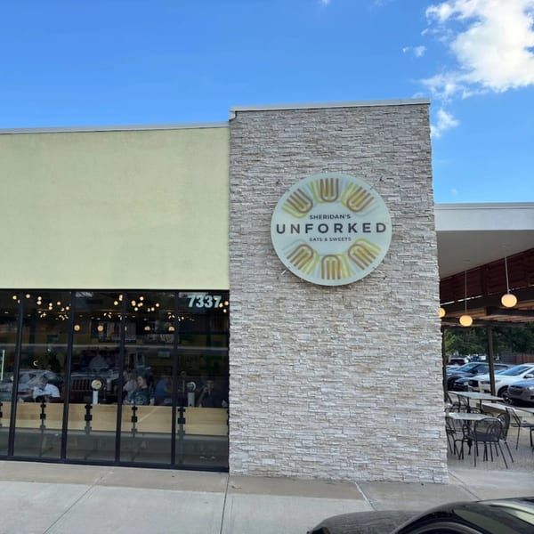 Exterior of Unforked restaurant with a large circular sign, outdoor seating, and visible interior.