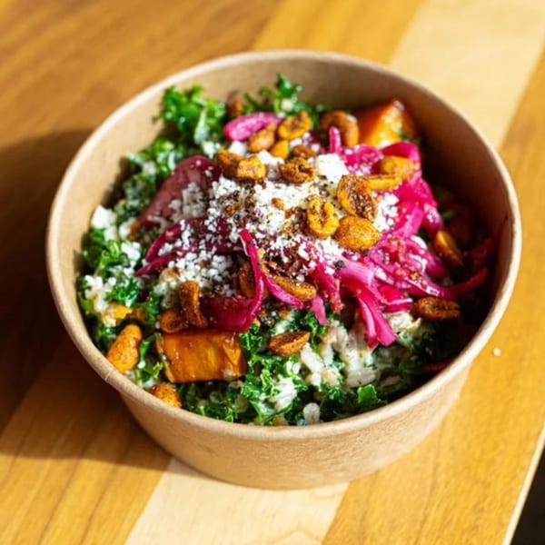 Unforked's kale salad with pickled onions, crumbled cheese, and roasted sweet potatoes in a bowl.