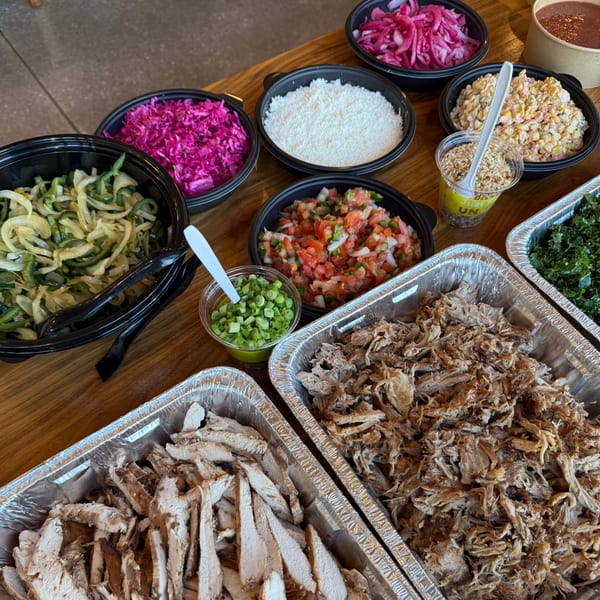 A buffet of burger toppings including shredded meats, pico de gallo, corn salad, and pickled cabbage.