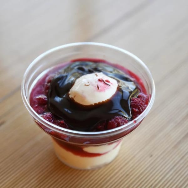 Unforked's raspberry parfait dessert in a clear cup, topped with chocolate sauce and cream.