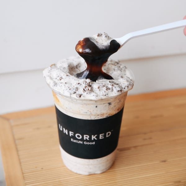A spoon drizzles chocolate sauce onto a creamy, cookie-filled Unforked milkshake.