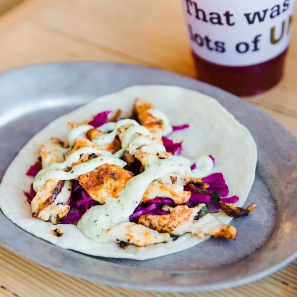 Unforked's chicken taco with purple cabbage and green sauce on a metal plate, with a drink in the background.
