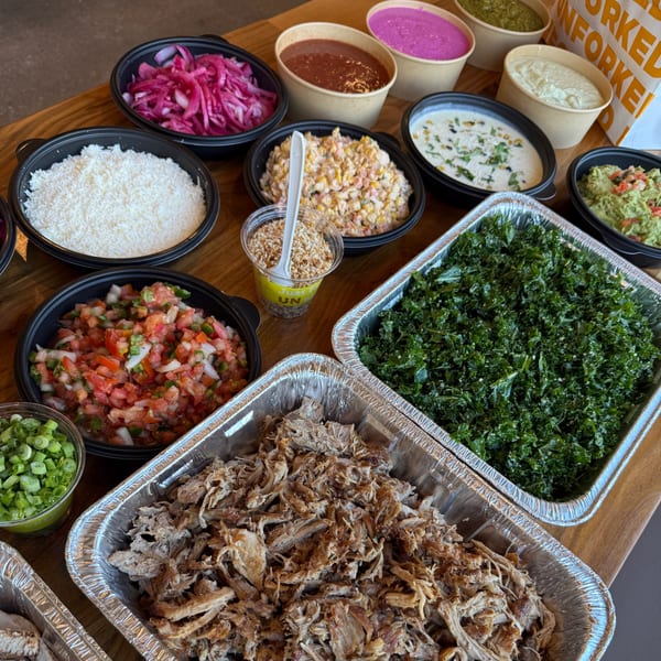 Unforked catering spread with pulled pork, kale, rice, salsa, guacamole, and various sauces.